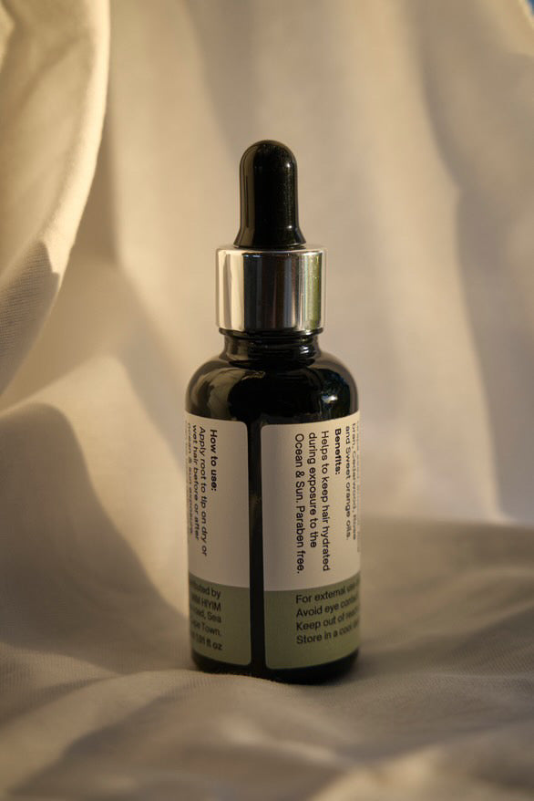 A bottle of hair oil with a dropper cap, labeled 'OCEAN LOVER', indicating the theme or preference of the product is for those who spend time near the ocean.