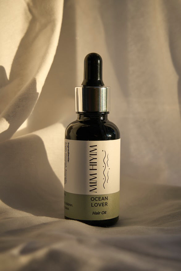 A bottle of hair oil with a dropper cap, labeled 'OCEAN LOVER', indicating the theme or preference of the product is for those who spend time near the ocean.