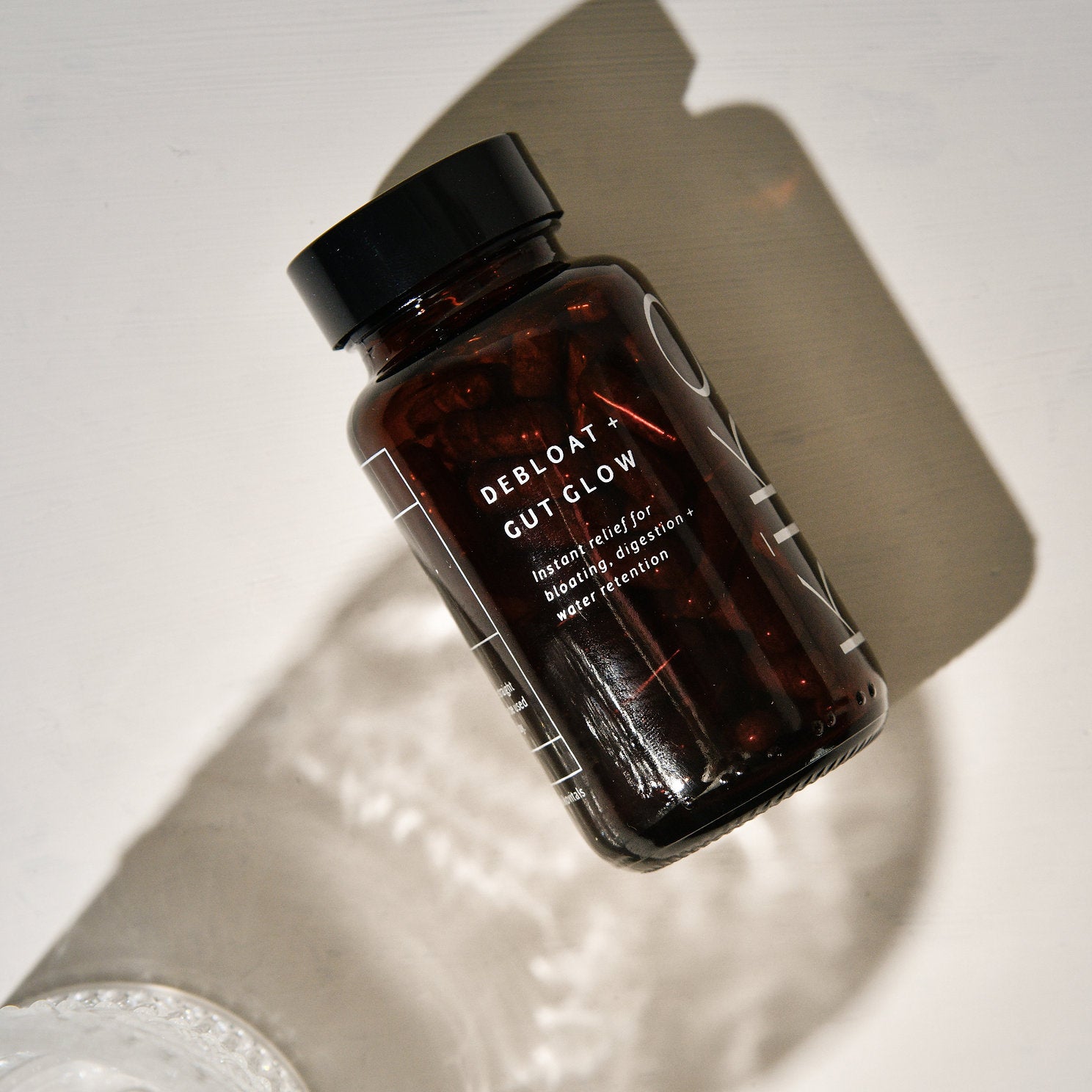 A brown bottle labeled 'DEBLOAT & GUTGLOW' with a black cap, placed on a surface with a shadow falling over it.