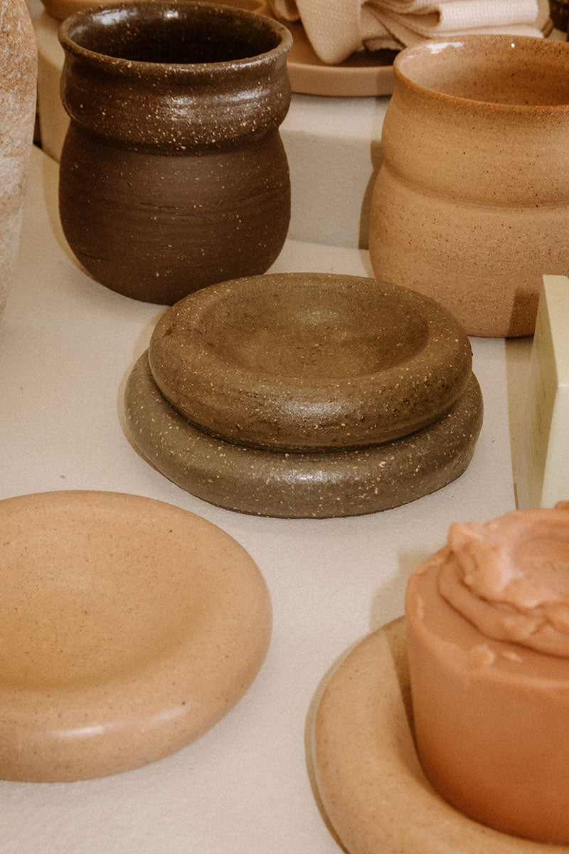 A handmade ceramic dish in a neutral color, displayed among other pottery pieces.