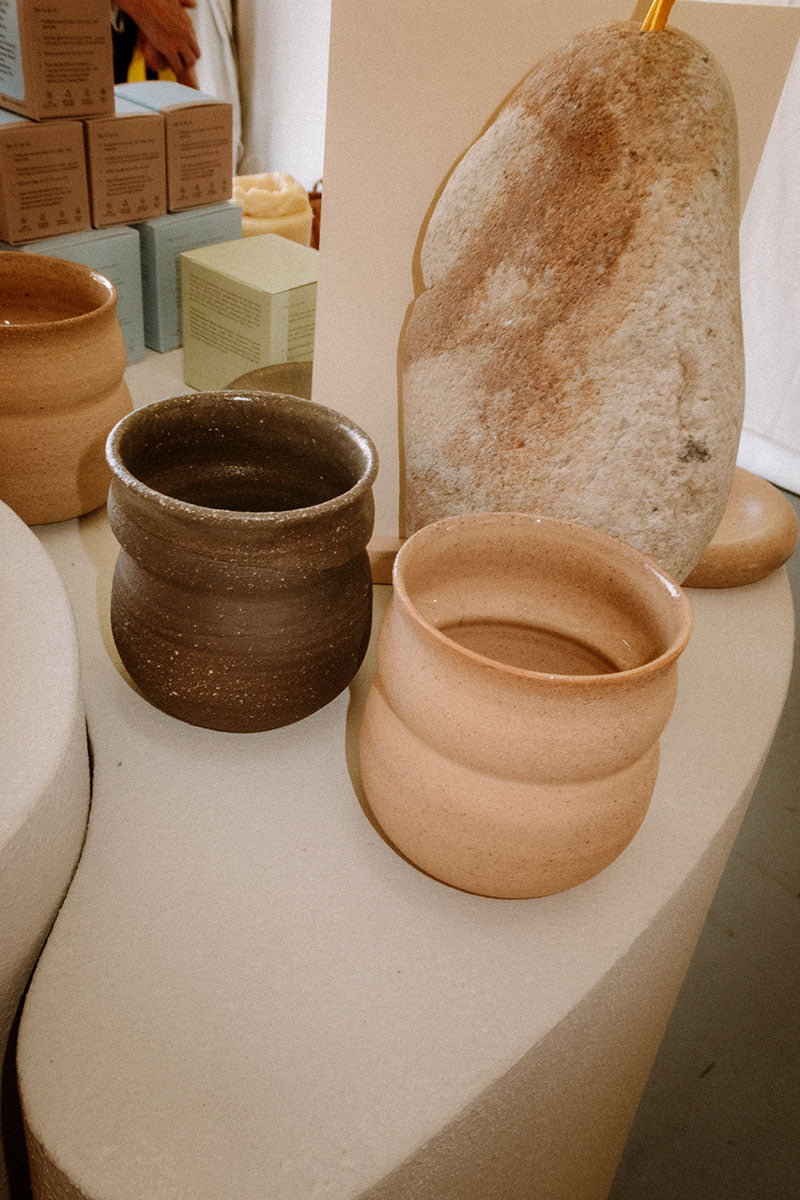 A ceramic mug in a beige color, displayed among other pottery pieces on a table.