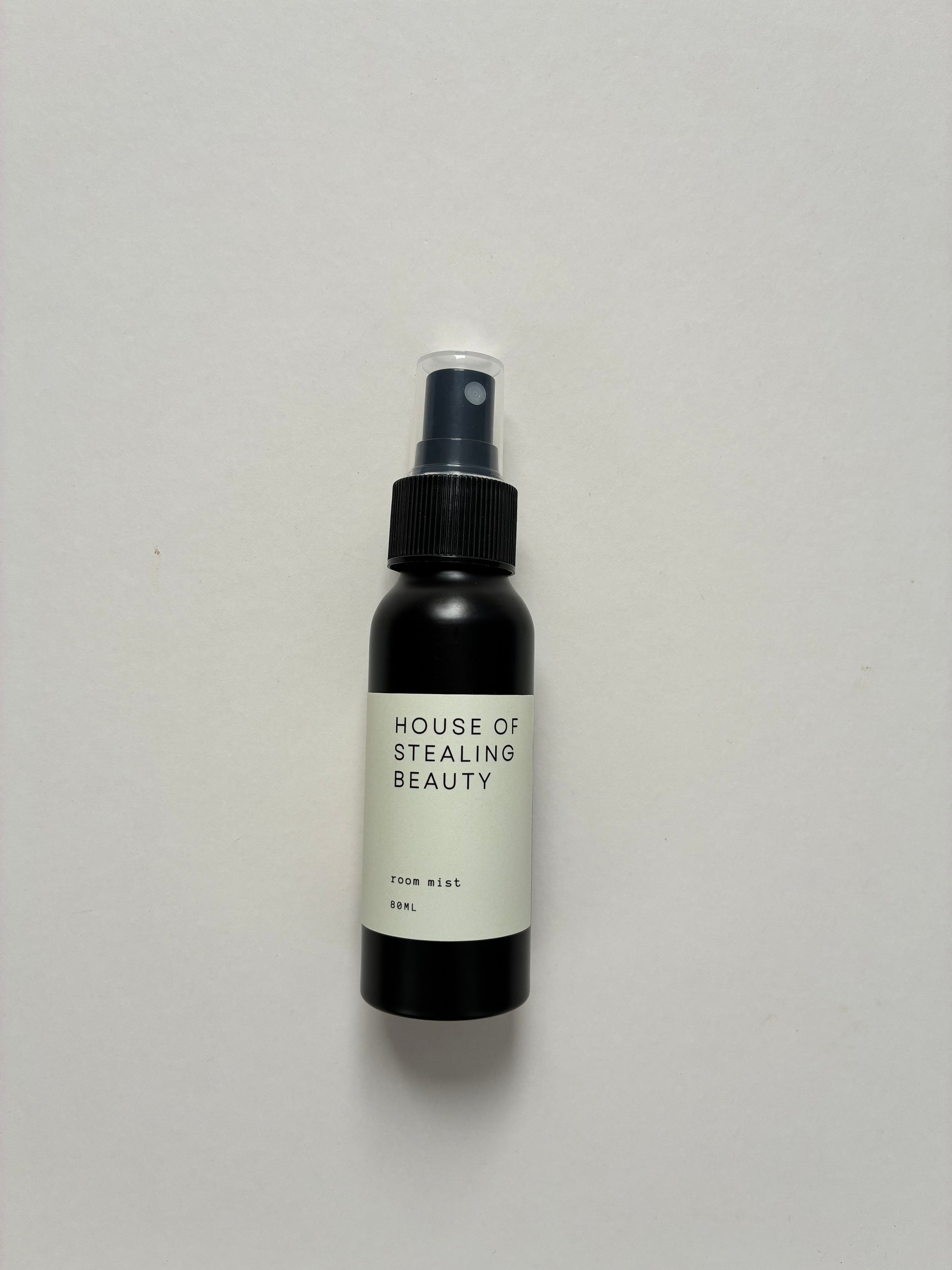 A small black spray bottle labeled 'HOUSE OF STEALING BEAUTY' with white text, standing against a white background.