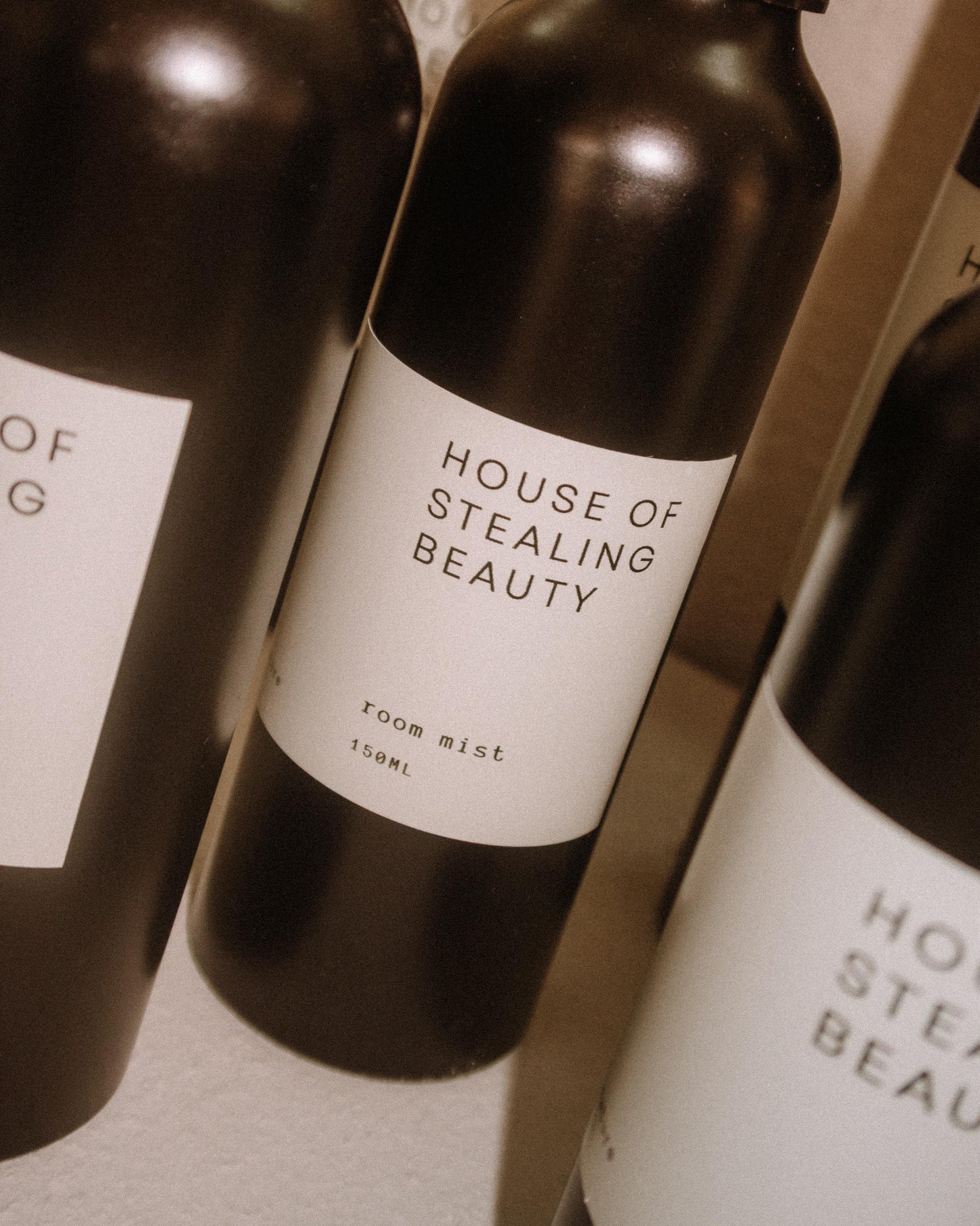 Bottle of 'House of Stealing Beauty' room mist, with a white label on a brown bottle, positioned on a shelf.